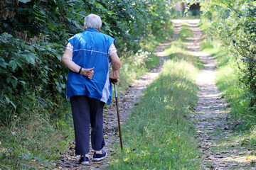 Old woman walking with a cane on a rural street. Limping person, diseases of the spine, life of elderly people