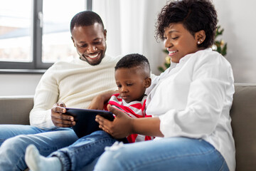 family, winter holidays and people concept - happy african american mother, father and baby son with tablet pc computer at home on christmas
