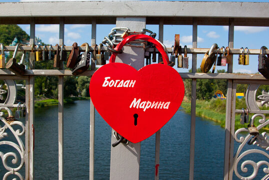 Ein rotes herzförmiges Schloss, das an einer Brücke in in der Ukraine hängt. Symbol der ewigen Liebe