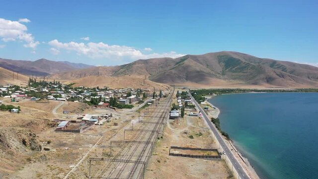 Aerial view empty Railway lines, traffic highway near  Sevan lake, Armenia. Drone fly over  Sevan town, blue lake,  train lines. In background mountains.