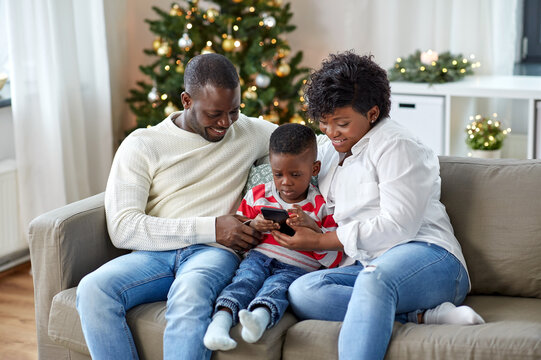 family, winter holidays and people concept - happy african american mother, father and little son with smartphone at home on christmas - Powered by Adobe