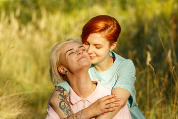 Lesbian happy loving red haired and blonde women spend time together sitting on green lawn in fresh spring garden at gentle sunlight closeup