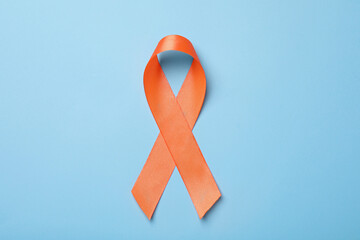 Orange ribbon on light blue background, top view. Multiple sclerosis awareness