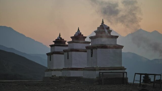 Muktinath temple stupas covered with smoke against misty mountains silhouettes at sunset, Nepal