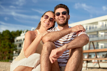 Obraz premium leisure, relationships and people concept - happy couple in sunglasses sitting on summer beach
