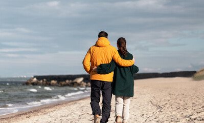 love, relationship and people concept - happy couple walking along autumn beach