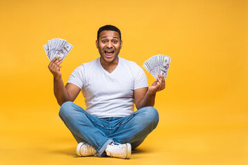 Portrait of african american indian black young man sitting on the floor holding dollar banknotes...
