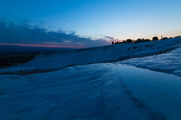 トルコ　夕暮れ時のヒエラポリス・パムッカレの石灰棚と青い水面