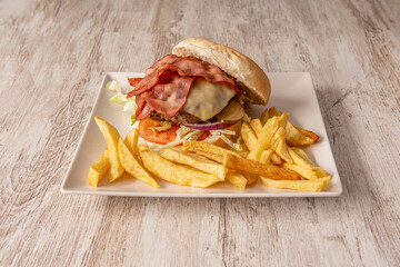 Beef burger with red onion, smoked bacon, pickled gherkins, lettuce and tomato with delicious homemade fries