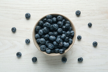 Ceramic bowl with blueberries on white wooden table, flat lay. Cooking utensil