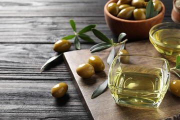 Glass bowls of oil, ripe olives and green leaves on black wooden table. Space for text
