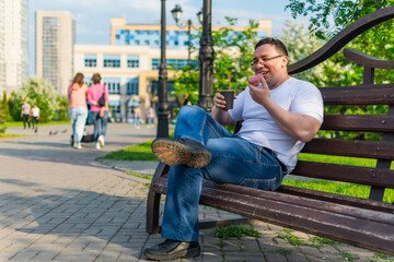 Happy man enjoying delicious donut and laughing while sitting on the bench