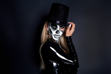 Beautiful model in Halloween makeup on black background. Sexy woman in top hat and skull makeup....