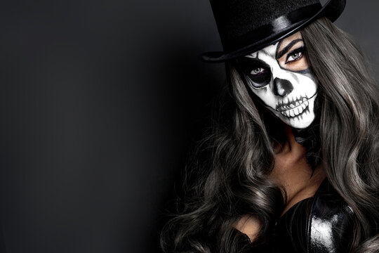 Beautiful model in Halloween makeup on black background. Sexy woman in top hat and skull makeup. Halloween makeup concept.