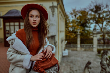Obraz premium Autumn fashion portrait of elegant woman wearing trendy autumn outfit with orange hat, turtleneck, sheepskin jacket, holding suede bag with fringes, posing in street of European city. Copy space