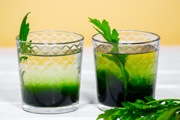 Green Chlorophyll or Chlorella drink in glass with water on white table, Orange Background. Green Drops in clear water, Antioxidant food and drinks.