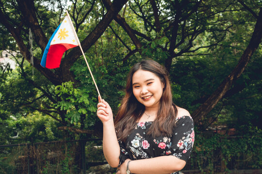 A cute and chubby Chinese Filipino woman proudly waving the Philippine flag. Outdoor patriotic scene.