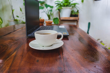 Coffee cup and laptop on a wooden table in the garden