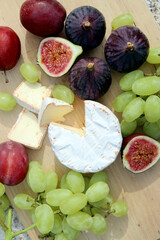 Still life with seasonal fruits and cheese. Close up photo of fresh figs, grapes, plums and cheese on wooden cutting board. Healthy eating concept. 