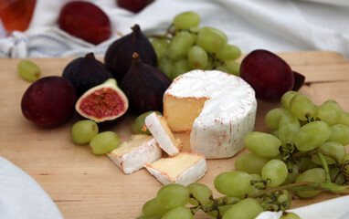 Cheese and fresh fruits on wooden board. Juicy figs, grapes and plums on a table. Gourmet food. 