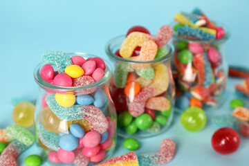 Fototapeta na wymiar Jars with different delicious candies on light blue background