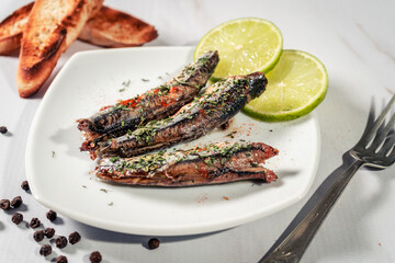 Appetizer of sardines in oil with parsley and paprika on a plate with some toast and lemon slices.