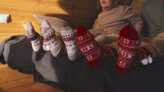 Close up handheld shot of mother, father and little daughter wearing warm festive socks sitting on bed in cabin