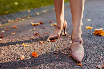 Close up of female shoes. Woman wears stylish brown high-heeled shoes in autumn park standing among falling leaves.