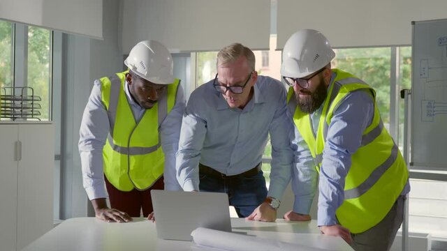 Architects discussing blueprint on laptop with construction manager in office