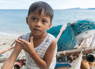 Fishing village boy playing in his grandfather's  banka fishing boat. A traditional fishing family net fishing from their home on the beach at  bignayan village, Philippines