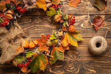 Close-up wreath autumn leaves and natural materials on rustic boards. Top view round wreath autumn harvest and foliage on brown wooden table. Thanksgiving day. Preparing for holiday. Copy space.