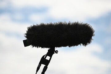 A professional directional microphone used by a camera team in front of a blue sky.
