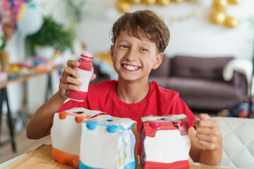 happy boy is sitting at the table drinking yogurt from a bottle and shows a thumbs up, a sign of...