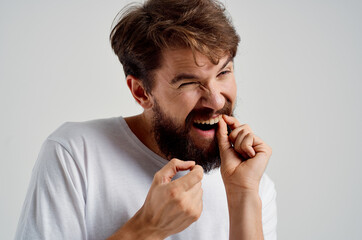 bearded man holding on to face pain in teeth light background