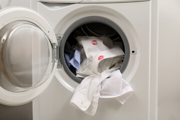 Men's shirt with lipstick kiss marks among other clothes in washing machine, closeup