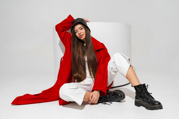 Fashionable  model in stylish  hat, red coat and boots  posing on white background in studio.