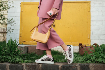 Street fashion elements: woman wearing trendy outfit with pink suit, zebra print sneakers, holding yellow faux leather handbag. Copy, empty space for text - 457551984