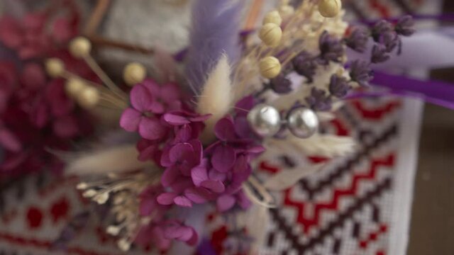 Bunch of dried lagurus flowers and purple flowers and silver balls. Decoration. Bouquet on an embroidered towel. Traditional Ukrainian ornament