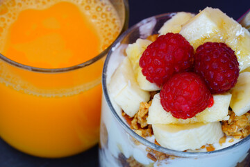 A yogurt parfait with granola and fresh raspberries and a glass of orange juice