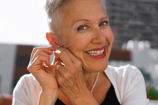 Close-up Photo Of A Happy Senior Woman Putting On The Earring.