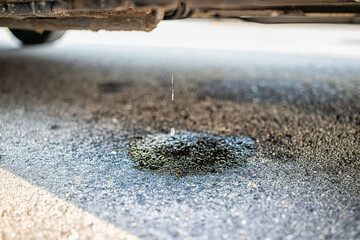 Parked car on street road with macro closeup of vehicle leaking fuel with puddle causing damage to...