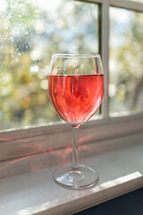 Closeup of one glass of wine drink or non-alcoholic diluted cherry or cranberry juice on windowsill window with sunlight and nature
