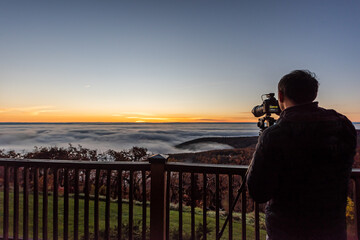 Wintergreen, Virginia ski resort town village with clouds fog mist inversion in Blue Ridge mountains at sunrise and man with camera photographer on apartment balcony