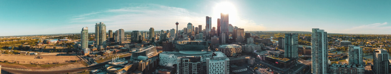 A panoramic image of downtown building and tower skyline against a shining sun and beautiful blue skies.