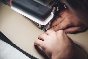 Working process of leather craftsman. Tanner sews leather on a special sewing machine, close up.