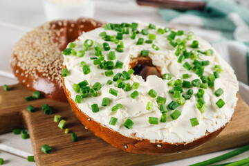 Delicious bagel with cream cheese and green onion on wooden board, closeup