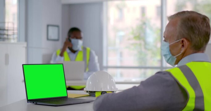 Side view of mature constructor in safety mask having video chat on laptop. Green screen
