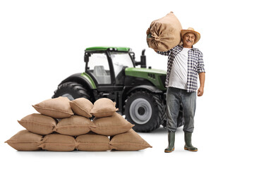 Full length portrait of a mature farmer with a tractor posing with a burlap sack on his shoulder