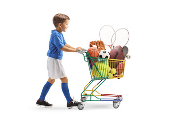 Full length profile shot of a boy in sports jersey pushing a mini shopping cart with sports...