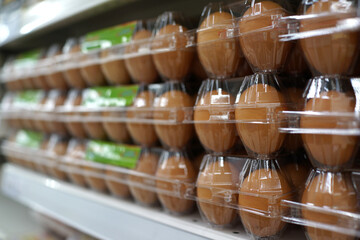 Stacks of brown eggs in a transparent plastic case display on the shelf in a grocery store.